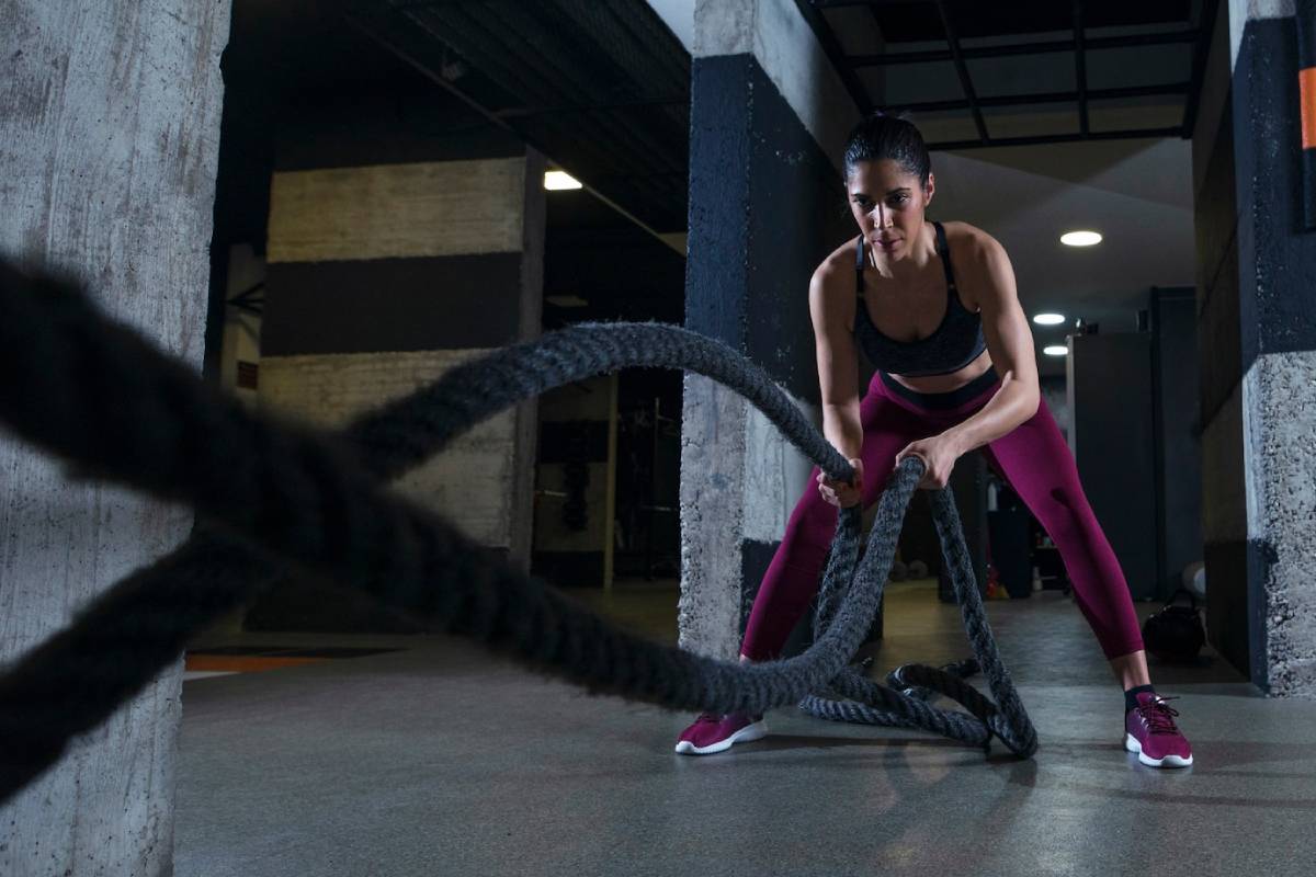 Woman exercising in a gym using heavy battle ropes, focused on her workout.