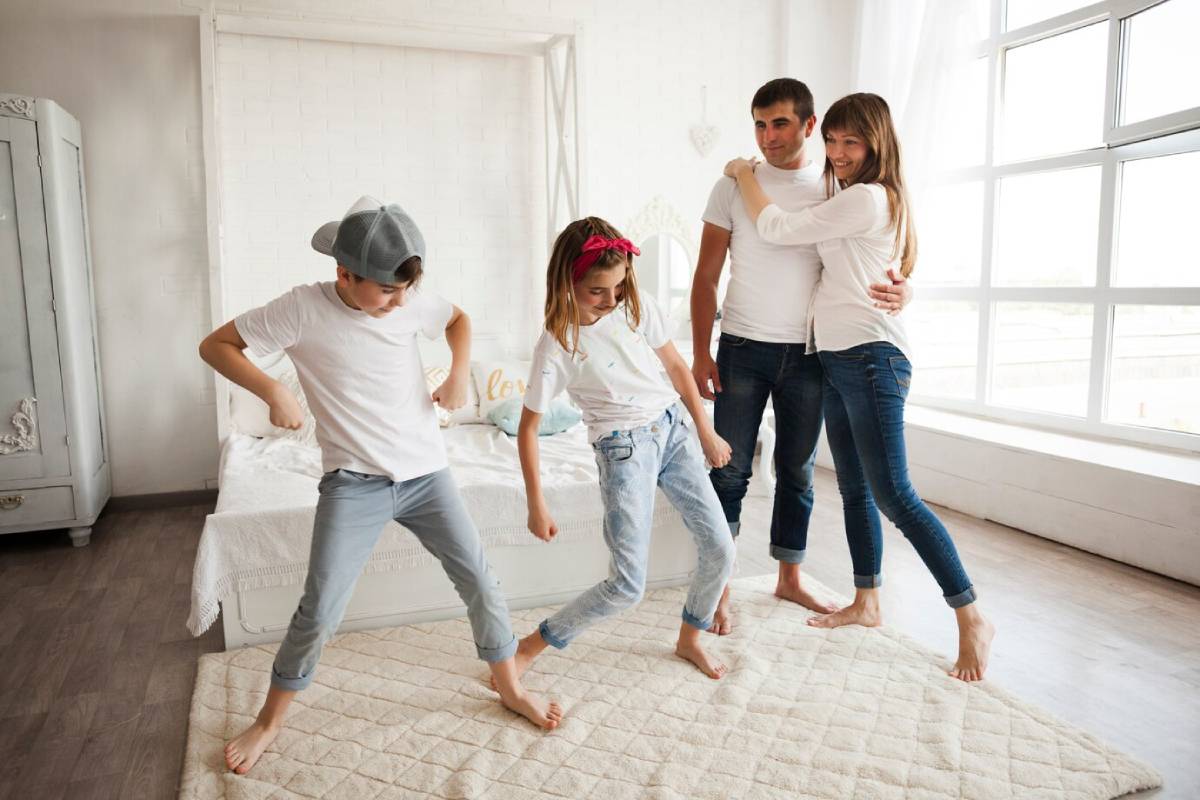 A family of four playfully dancing in a bright, airy bedroom.