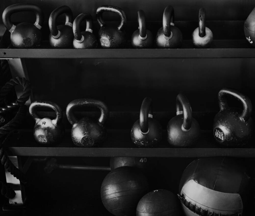 Monochrome image of assorted kettlebells on gym racks, along with exercise balls beneath.