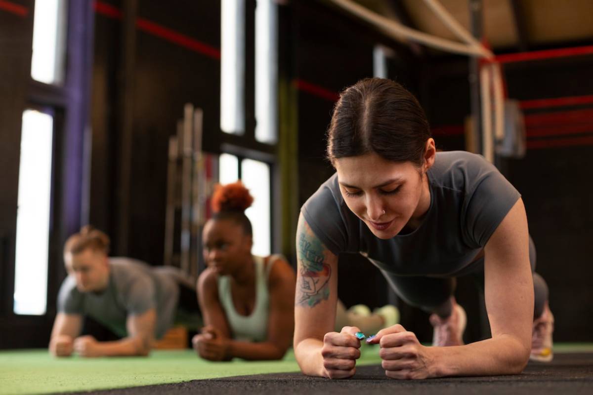 Three women of diverse backgrounds doing plank exercises in a gym, focusing intently on their workout.