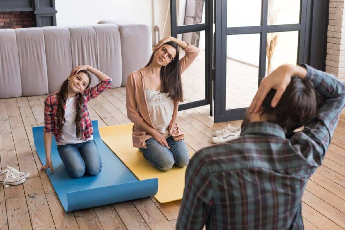 A man photographs two women posing playfully on yoga mats indoors.