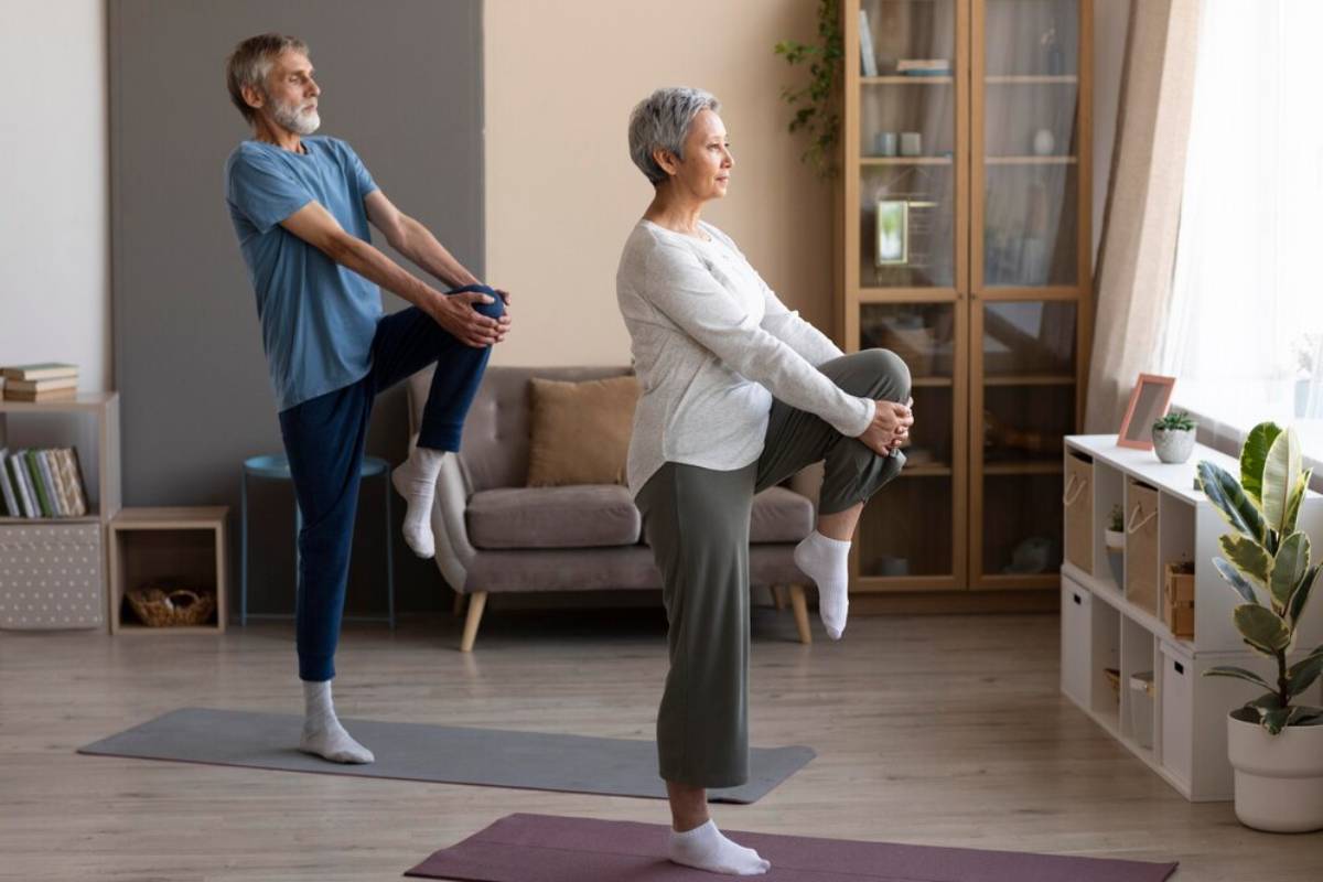 An elderly couple practicing yoga together in their living room, stretching on individual mats.