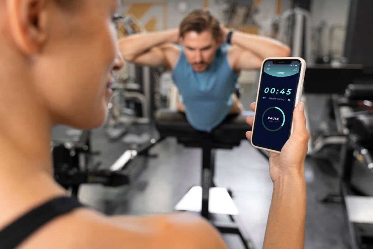 A woman in a gym timing a man's workout session using a smartphone app.