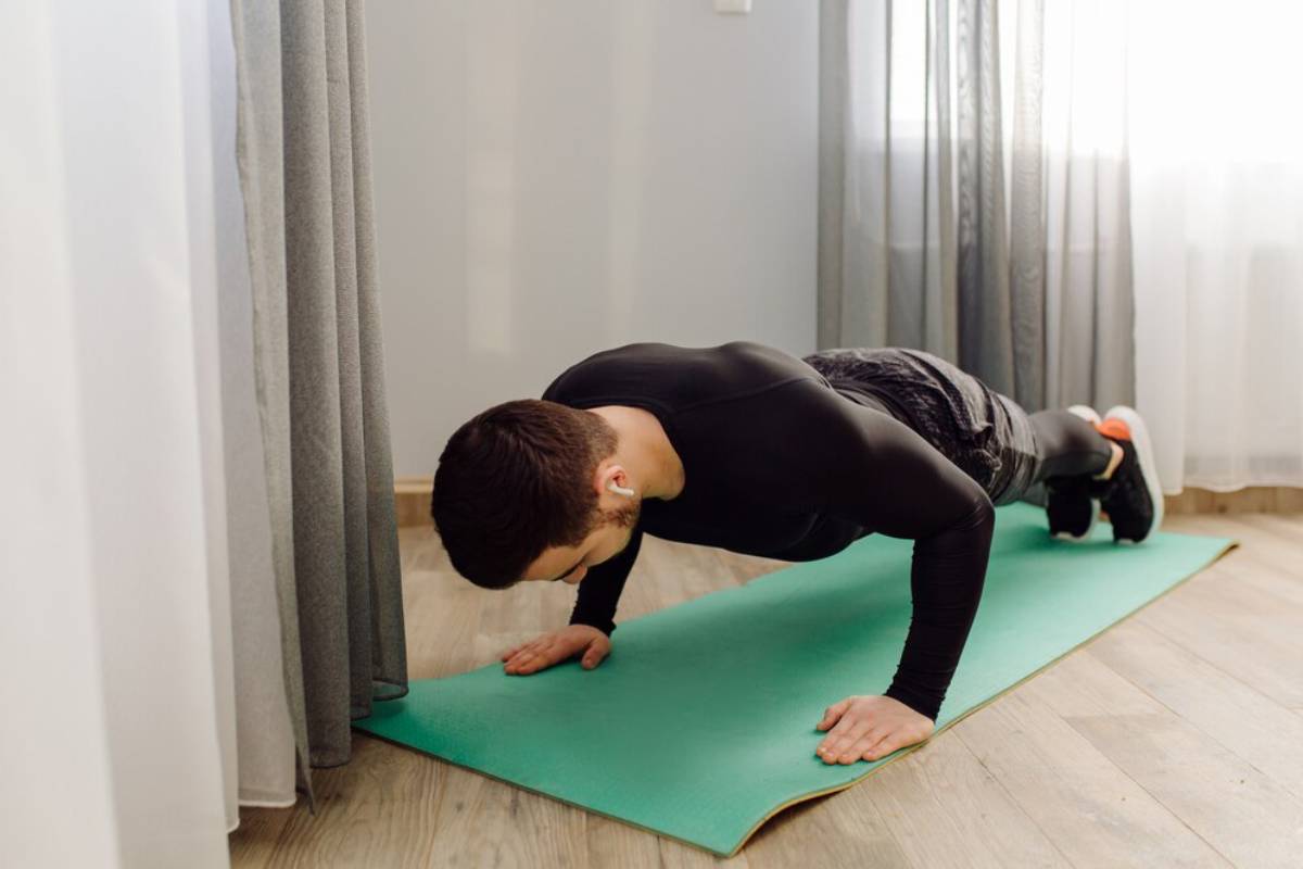 Man in black activewear doing a plank on a green yoga mat indoors.