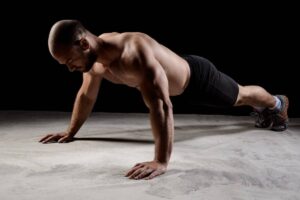 A man performing a push-up in a gym setting, showcasing muscular physique and focus.