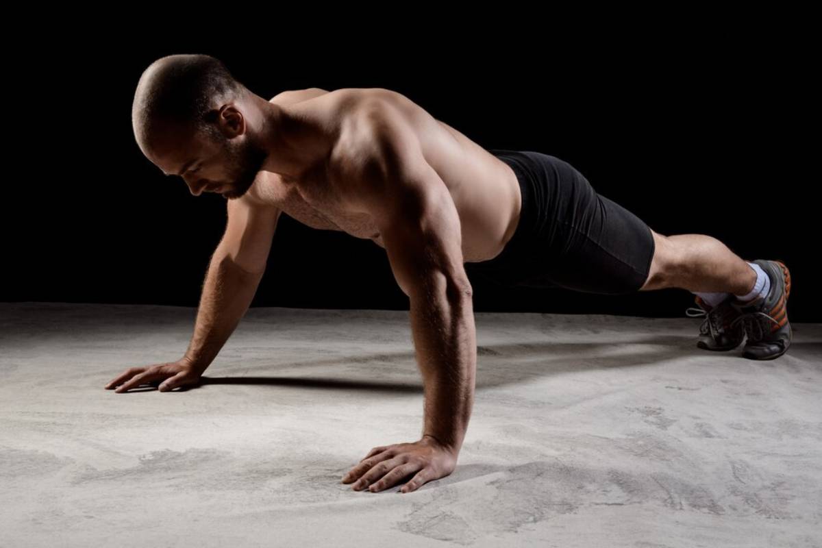 A man performing a push-up in a gym setting, showcasing muscular physique and focus.